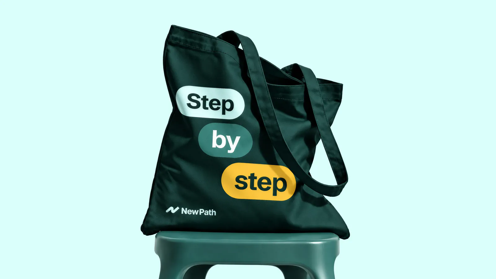 Tote bag reading Step by step in pill-shaped labels, on a stool against pale mint
